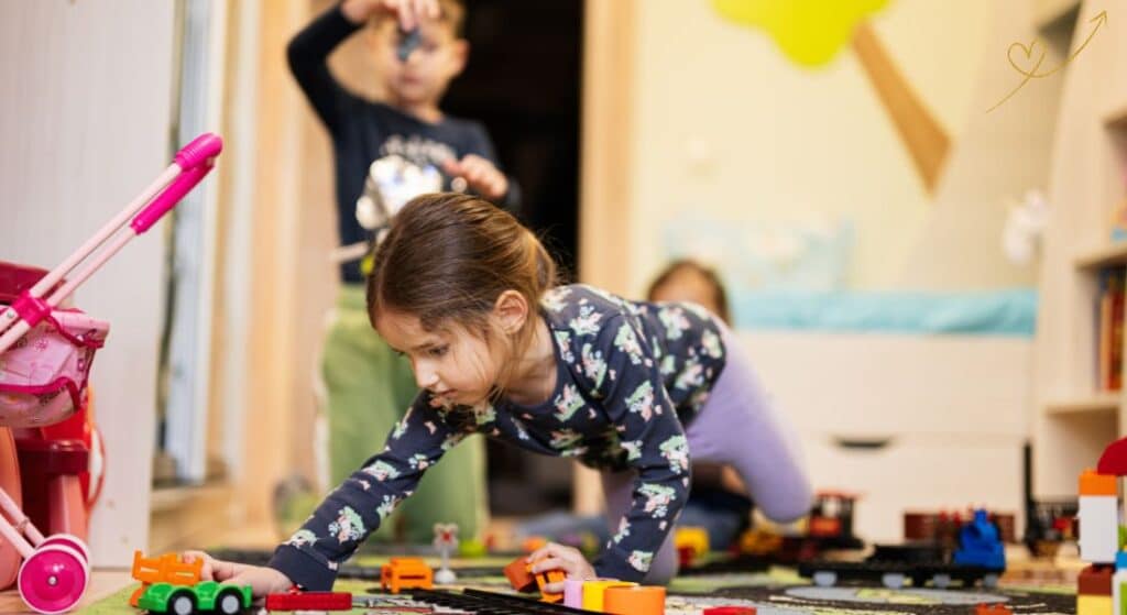 Duas meninas e um menino brincando de forma criativa com carrinhos, pista , obstáculos e muita criatividade.