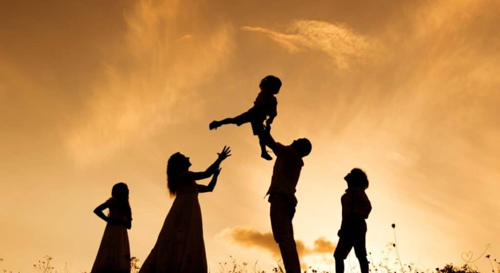 Família ao pôr do Sol retratada pela mãe, pai segurando filho mais novo para o alto, acompanhados por mais dois filhos uma menina e um menino.