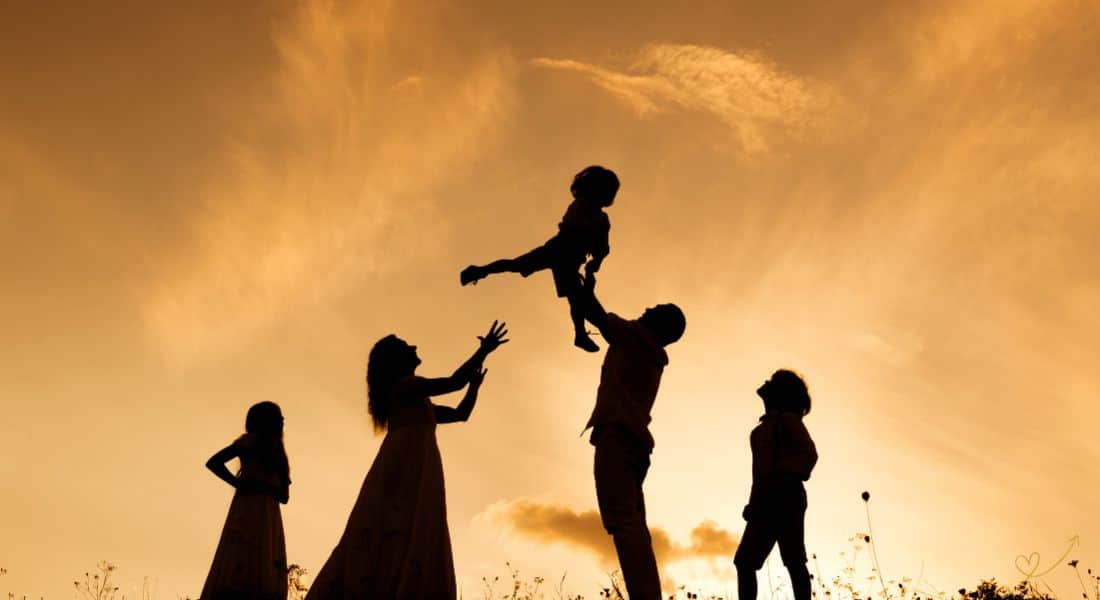 Família ao pôr do Sol retratada pela mãe, pai segurando filho mais novo para o alto, acompanhados por mais dois filhos uma menina e um menino.