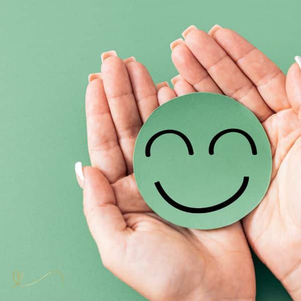 Uma Mão segurando um emoji na cor verde com um sorriso