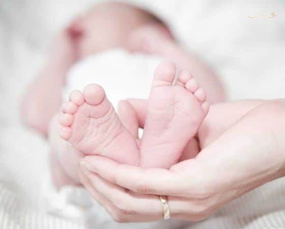 Amor-e-cuidado bebê deitado com os pés voltados para a câmera e sua mãe segurando-os juntos de forma carinhosa.
