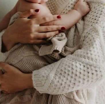 Mãe-e-filho Uma mãe vestindo uma blusa de tricô bege claro segurando seu bebê no colo