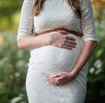 Maternidade-Amor Mulher grávida vestindo um vestido de renda branco segurando sua barriga de forma carinhosa e protetora