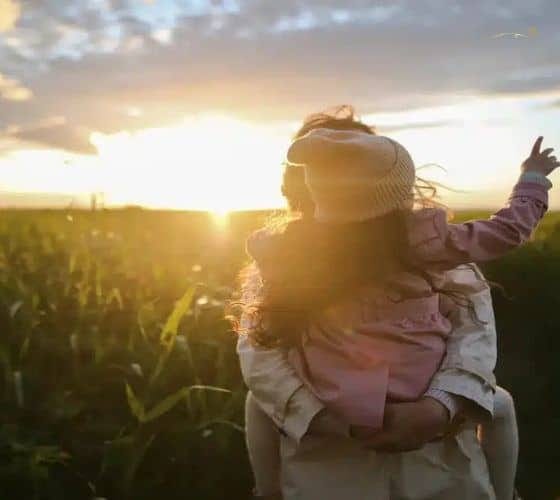 Uma Mãe e sua filha abraçadas como por do sol abraçando-as.