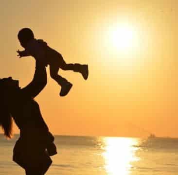 amor de mãe Mãe brincando com seu filho ao pôr do Sol em uma praia.