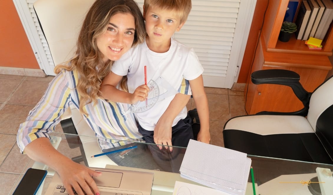 10 Dicas de organização para mães empreendedoras em casa mãe em seu escritório dentro de casa, com seu filho sentado no colo e trabalhando no seu notebook.