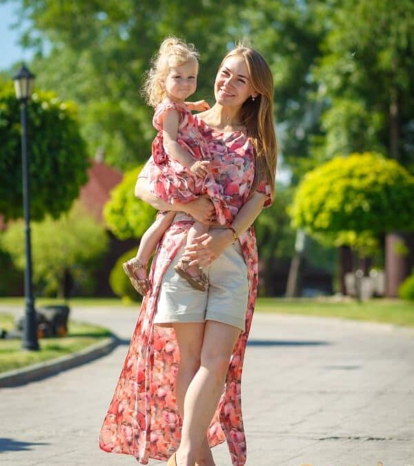 Mãe e filha usando roupas florais rosa claro em um jardim ensolarado, sorrindo com leveza.